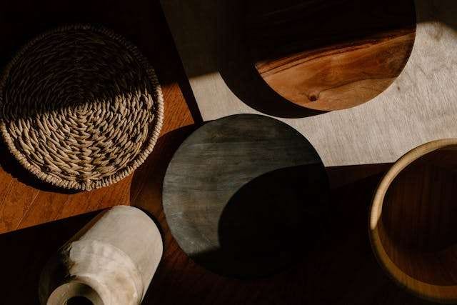 Woven and wooden decor pieces casting shadows across a wood surface.