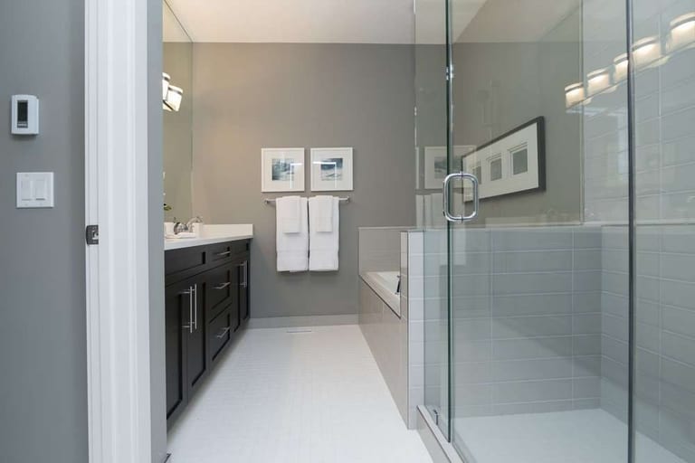A glass-walled shower enclosure in a grey bathroom with a dark vanity and pale tile flooring