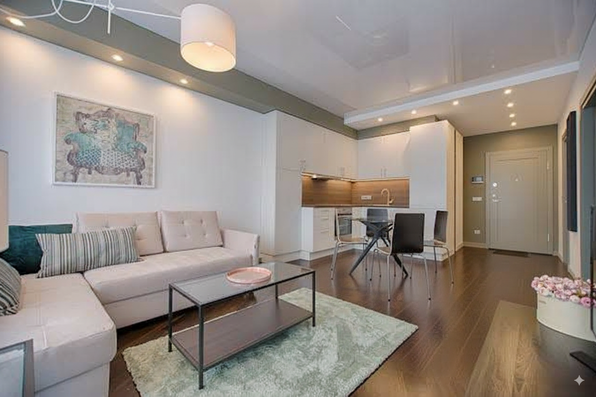A living room with a dark hardwood floor, a cream sectional and an open kitchen behind.
