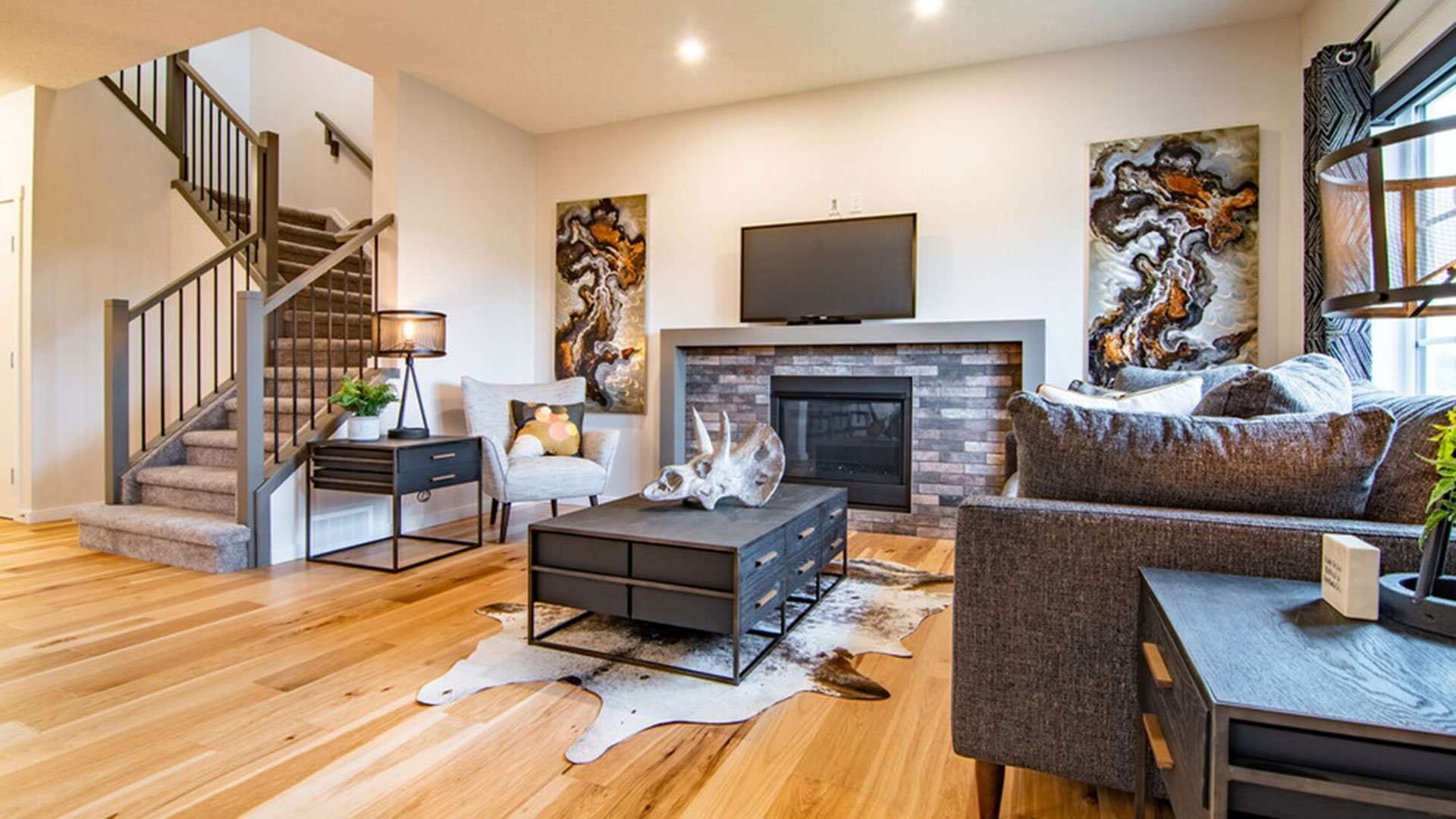 An open living and dining area with natural-toned hardwood running throughout, a brick-faced fireplace, an open staircase and a hide rug.