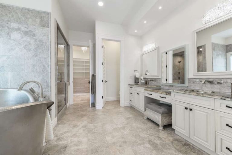 Grey stone-look tile flooring in a bright ensuite with a freestanding tub and a long double vanity.