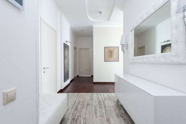 A white hallway with a dark wood floor and a patterned grey runner.