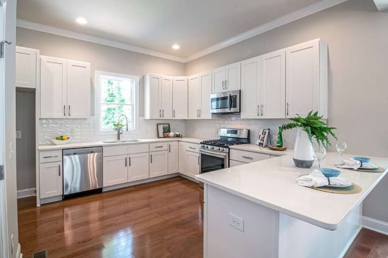 Medium-brown wood flooring in a white kitchen with shaker cabinets and stainless steel appliances
