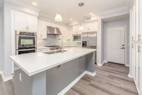 A white kitchen with a long island and grey wood-look plank flooring.