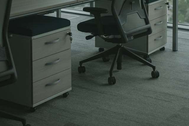 Office chairs and filing pedestals on grey carpet tile.