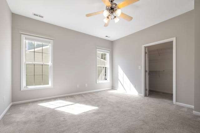 An empty bedroom with light grey carpet and a ceiling fan.