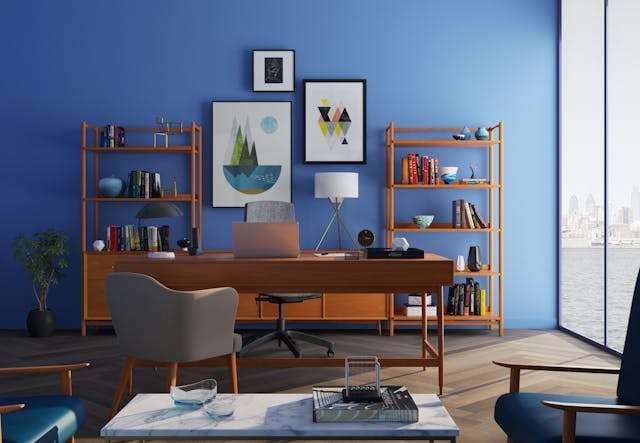 A blue-walled home office with a wooden desk, shelving and a herringbone wood floor.